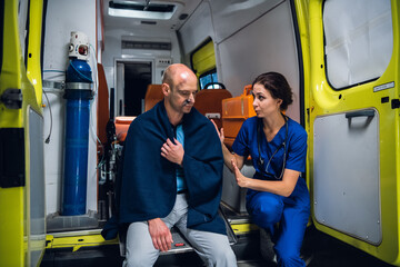 Ambulance car, nurse calms down an injured man in a blanket.