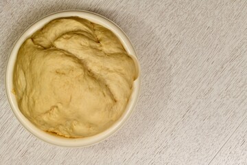  The puffed yeast dough has risen in a light, round bowl on the left, on the countertop with a diagonal patina pattern.
