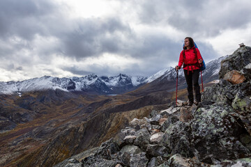 Fototapeta premium Girl Backpacking along Scenic Hiking Trail surrounded by Mountains in Canadian Nature. Taken in Tombstone Territorial Park, Yukon, Canada.