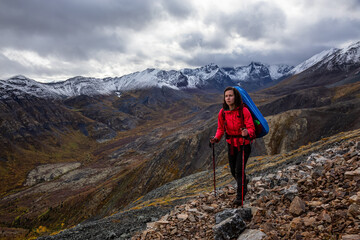 Fototapeta na wymiar Girl Backpacking along Scenic Hiking Trail surrounded by Mountains in Canadian Nature. Taken in Tombstone Territorial Park, Yukon, Canada.