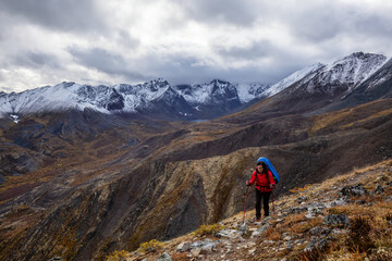 Fototapeta na wymiar Girl Backpacking along Scenic Hiking Trail surrounded by Mountains in Canadian Nature. Taken in Tombstone Territorial Park, Yukon, Canada.