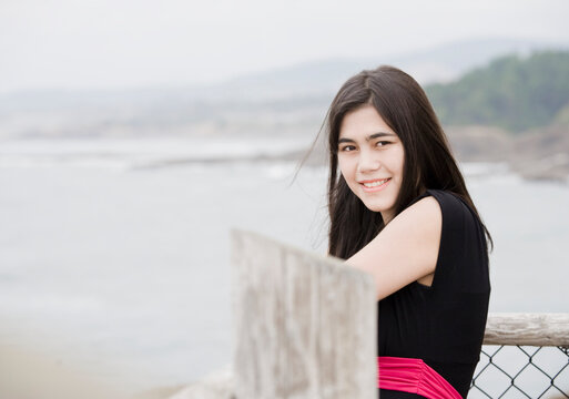 Elegant Young Woman Or Teen Standing By Ocean In Simple Black Dr