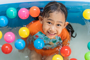 Fototapeta na wymiar Asian little girl playing with in the pool at house and coloured balls