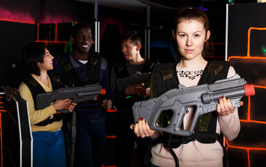 Portrait of confident female laser tag player with gun ready for game in dark room