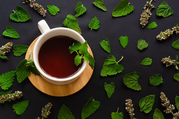 cup of black tea with mint leaves  on wooden saucer on black background. Top view