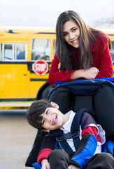 Big sister with disabled brother in wheelchair by school bus © Yay Images