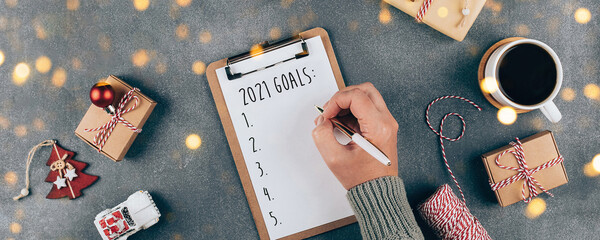 Happy New Year 2021. Woman's hand writing 2021 Goals in notebook. Top view, flat lay. Banner