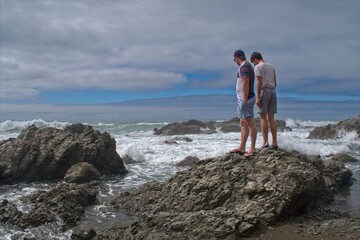 Two Young Men Standing on Rocks Watching the Surf