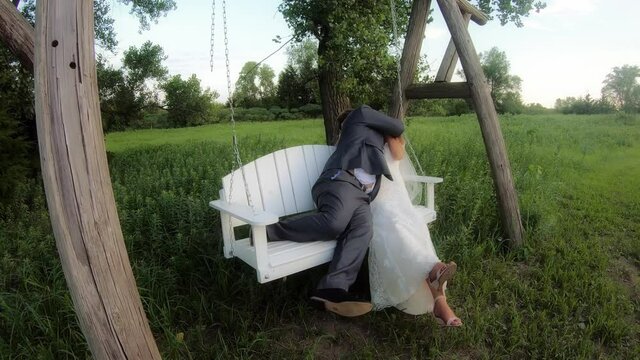 A groom being silly with his bride on a white bench swing in a field
