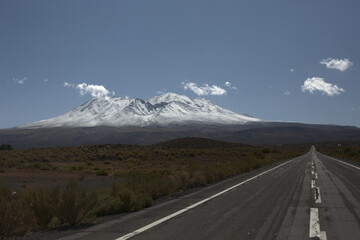 Snowy Andes' volcano mountain on the background from a high altitude chilean road towards Argentina in a shiny bright blue sky day.