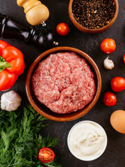 fresh raw minced pork in a wooden bowl with vegetables on the ba