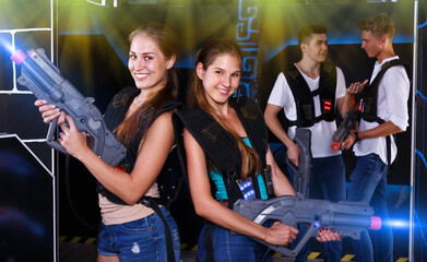 Fototapeta na wymiar Portrait of two positive girls with laser pistols in their hands in dark laser tag room