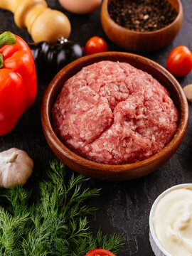 fresh raw minced pork in a wooden bowl with vegetables on the ba
