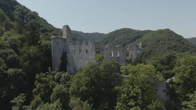Drone shot flying out through cracked wall of heritage old castle surrounded by green trees and mountains