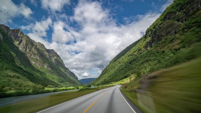 A drive on the E39 freeway in Norway near Byrkjelo. The Road is running through the lush green walley. Farms and small villages scattered on the valley floor. Mountains towering above the.