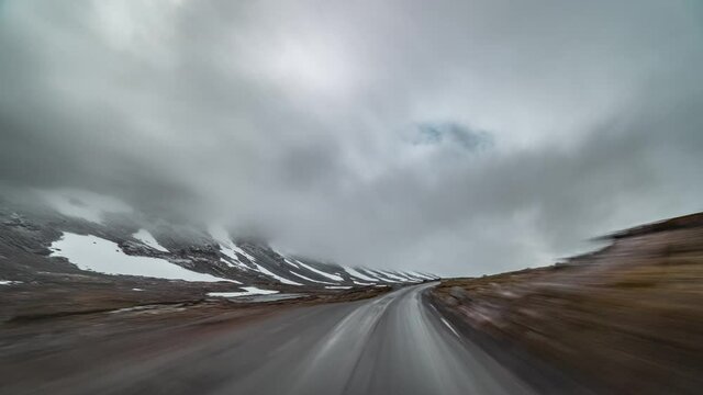 A drive on the mountaineous plateau on country road 258 towards Stryn, Norway. Thick white-gray clouds hanging above. Harsh tundra landscape is on the both sides of the road. Rain stats to fall.