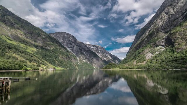 The beautiful view of the Naeroy fjord from Bakka. High mountains, partly covered with forest, are reflected in the mirrorlike surface of the fjord. White clouds passing above casting shadows.