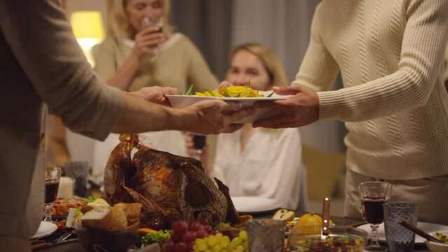 Two men setting Thanksgiving dinner table while two relaxed women looking at them and drinking red wine
