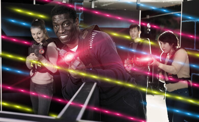 Emotional African man with a laser pistol playing laser tag with friends on dark labyrinth