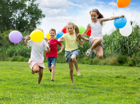 happy playful elementary school age boy and girls with air balloons in hands running in summer park. Selective focus .