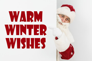 Santa Claus points his fingers at the board with the text - WARM WINTER WISHES