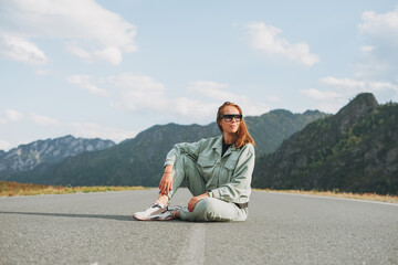 Fototapeta premium Beautiful smiling young woman traveler in casual clothes on road, trip to mountains