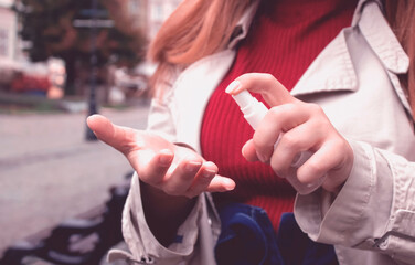 Closeup image of young adult woman using sanitizer or disinfectant spray walking the street....