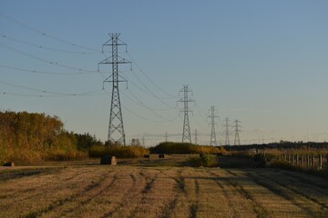 Power lines with a dirt road and round bales at sunset in Autumn.