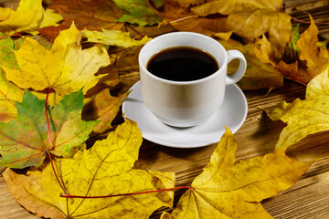 Cup of coffee and autumn maple leaves on wooden table. Autumn concept