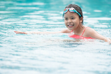 smiling child wearing swimming glasses in swimming pool. little girl playing in outdoor swimming pool on summer vacation on tropical beach island. child learning to swim in pool of luxury resort.
