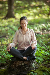 Young woman wearing yoga pants meditating in the woods on a sunny morning.