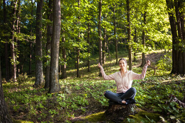 Naklejka na ściany i meble Young woman wearing yoga pants meditating in the woods on a sunny morning.