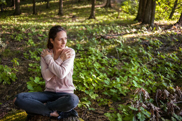 Young woman wearing yoga pants meditating in the woods on a sunny morning.