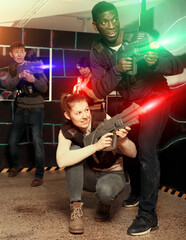 Fototapeta na wymiar Nice laser tag players of different nationalities aiming laser guns at other players during lasertag game in dark room
