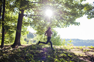 Young woman wearing yoga pants meditating in the woods on a sunny morning.