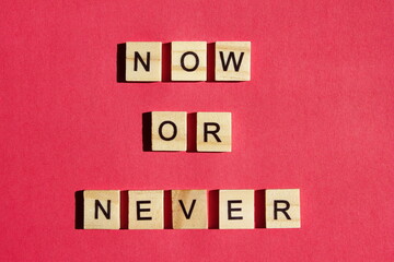 Now or never - the motivating inscription is laid out on a red background with wooden blocks with black letters. Call to action.