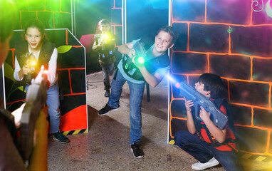 Obraz na płótnie Canvas Group of happy pleasant teenagers with laser guns having fun on dark lasertag arena