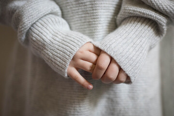 Hands of a small child clasped together with light grey woven jumper