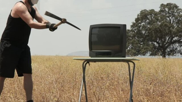 Man smashing old TV with pickaxe. Destroying analog television in slow motion
