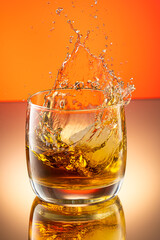 whiskey with ice splash in a glass on a colored gradient background
