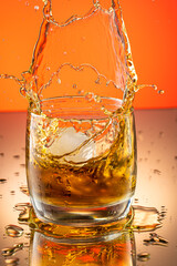 whiskey with ice splash in a glass on a colored gradient background