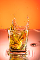 whiskey with ice splash in a glass on a colored gradient background