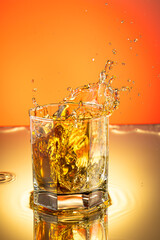 whiskey with ice splash in a glass on a colored gradient background