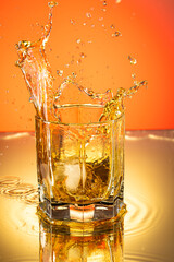 whiskey with ice splash in a glass on a colored gradient background