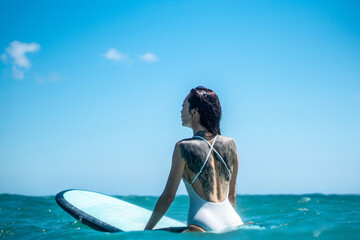 Portrait of surfer girl with tattoo on surf board in blue ocean