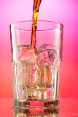 pour cola into a glass with pieces of pure real ice on a red purple gradient background