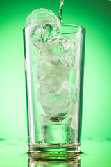 pouring green tarragon lemonade into glass with pieces of pure real ice on green gradient background