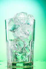 pouring green tarragon lemonade into glass with pieces of pure real ice on green gradient background