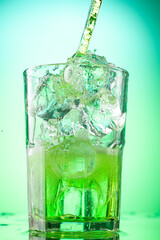 pouring green tarragon lemonade into glass with pieces of pure real ice on green gradient background