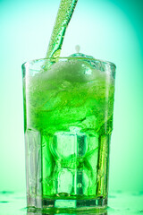 pouring green tarragon lemonade into glass with pieces of pure real ice on green gradient background
